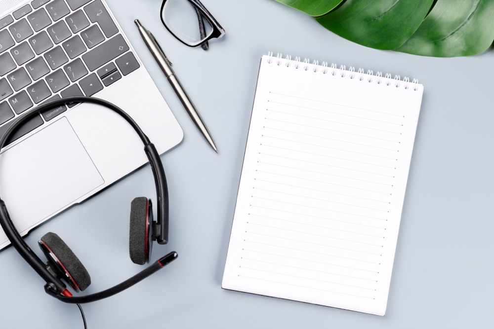 Laptop, Headset und Notizblock auf einem Schreibtisch